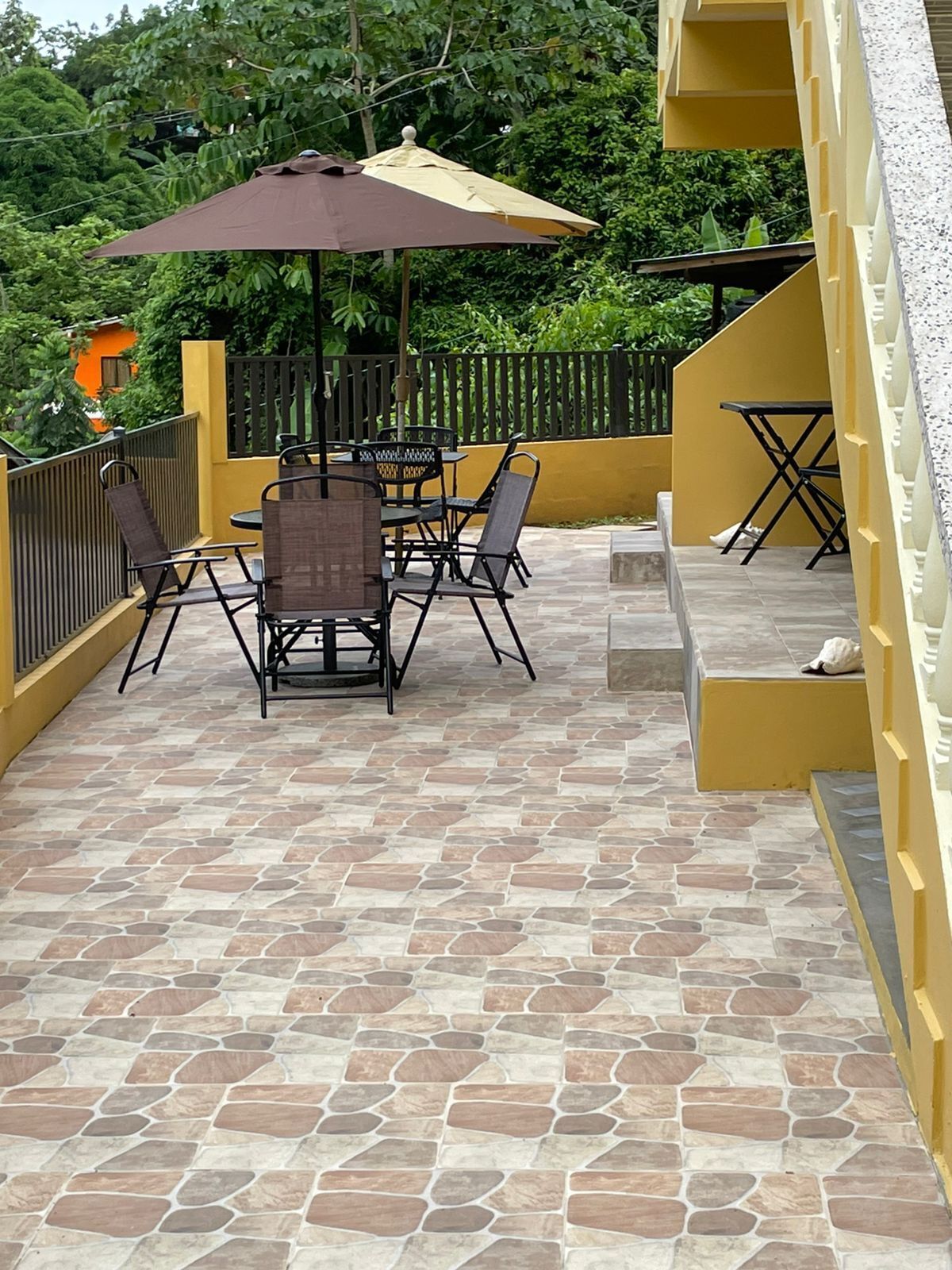 Eine Terrasse mit Steinboden, einem Tisch mit Stühlen und einem großen Sonnenschirm.