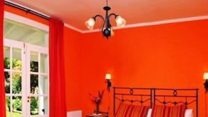Quarto com cama, janela com cortinas, mesa de cabeceira com abajur e lustre.