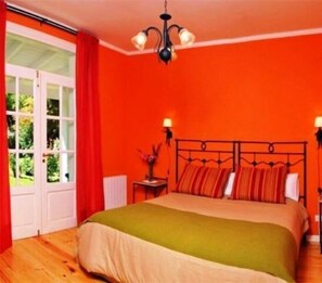 Une chambre à coucher avec un lit, une fenêtre avec des rideaux, une table de chevet avec une lampe et un lustre.
