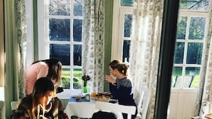 Uma área de refeições com uma mesa posta para dois, uma janela com cortinas e vista para o verde lá fora.