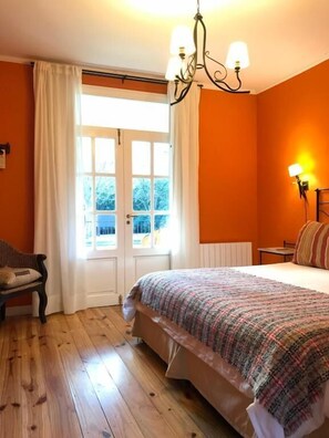 Une chambre à coucher avec un lit, une chaise, une fenêtre avec des rideaux et une lampe fixée au mur.