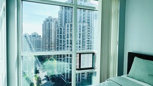 A bedroom with a large window, a bed, and a view of high-rise buildings. - Cozy Vibes Condo (Toronto)