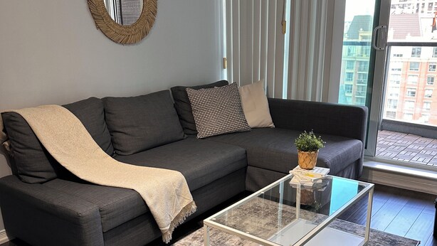 A modern living room with a dark grey sofa, a glass coffee table, and a patterned rug. - Cozy Vibes Condo (Toronto)