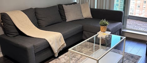 Un salon moderne avec un canapé gris foncé, une table basse en verre et un tapis à motifs.