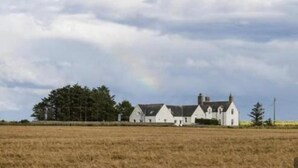 Uma fileira de casas brancas com um amplo campo em primeiro plano e um céu parcialmente nublado.