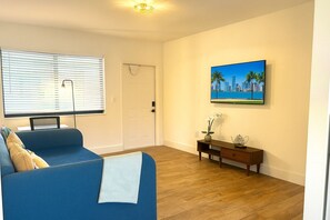 A living room with a blue sofa, a wooden coffee table, a TV mounted on the wall, and a door with a towel hanging on it. - U2 Cozy 1-Bedroom Miami · A/C & Parking · Steps from Vizcaya Metro and Brickell (Miami)