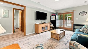 Een woonkamer met een televisie, houten meubels, een bank en een deur naar een balkon.
