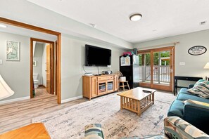 A living room with a television, wooden furniture, a sofa, and a door leading to a balcony. - 1819 - Always Dreaming Spacious 5BR Corolla retreat with pool, hot tub, and beach access. (Corolla)