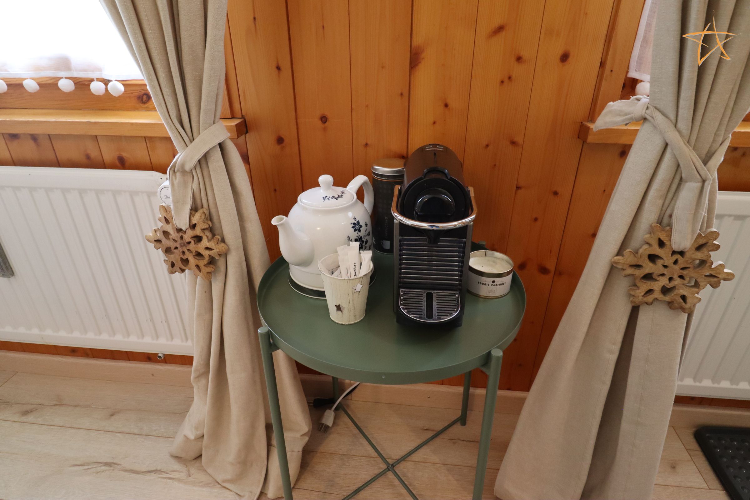 A room with a wooden floor, a table with a kettle, a coffee maker, a cup, and a container.