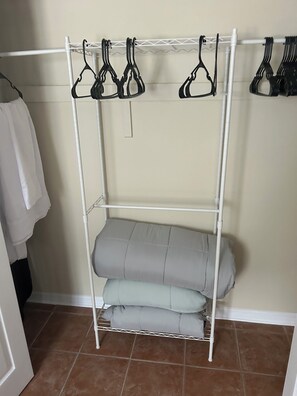 Ein weißer Metallschrank mit mehreren Einlegeböden und Kleiderstange, in einem Raum mit Fliesenboden.