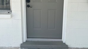 A gray door with the number 2, a window with floral curtains, and a small step leading to the entrance. - Cozy 1-bedroom apartment in peaceful St. Pete Beach with AC (St. Pete Beach)