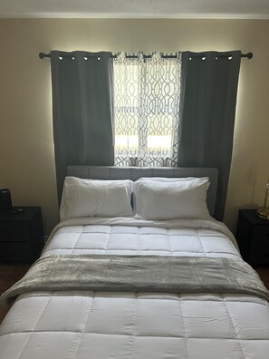 Ein Bett mit weißer Bettwäsche, ein Fenster mit gemusterten Vorhängen und zwei Nachttische.