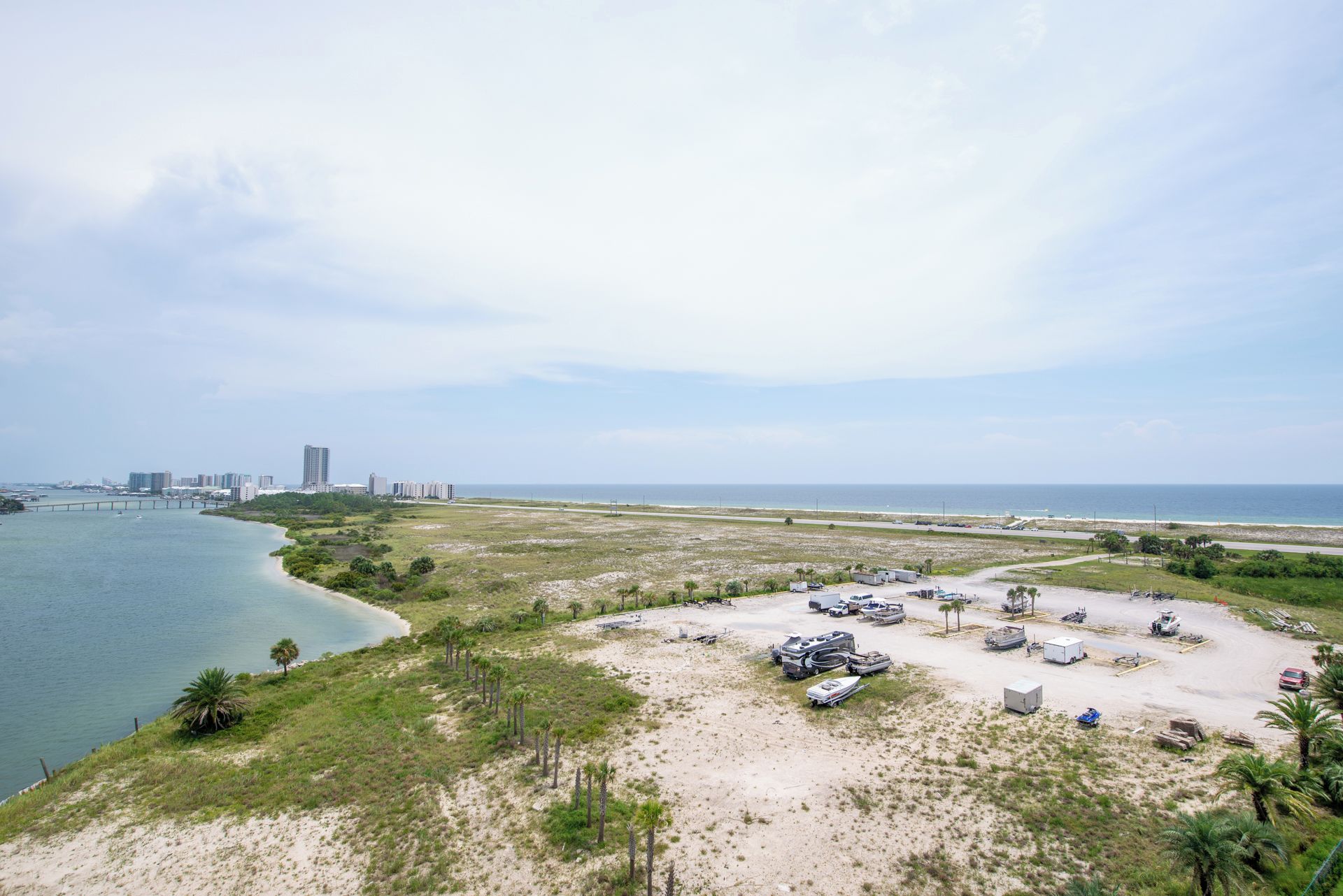 An aerial view of a coastal area with a beach, a parking lot, and a bridge in the distance.
