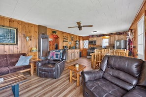 A cabin interior with a wooden floor, leather sofas, a dining area, and a kitchen.