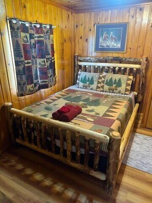 Uma cama com estrutura de madeira, um edredom, uma manta vermelha e um quadro na parede.