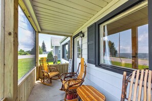 A covered porch with wooden chairs and a rocking chair, overlooking a residential street.
