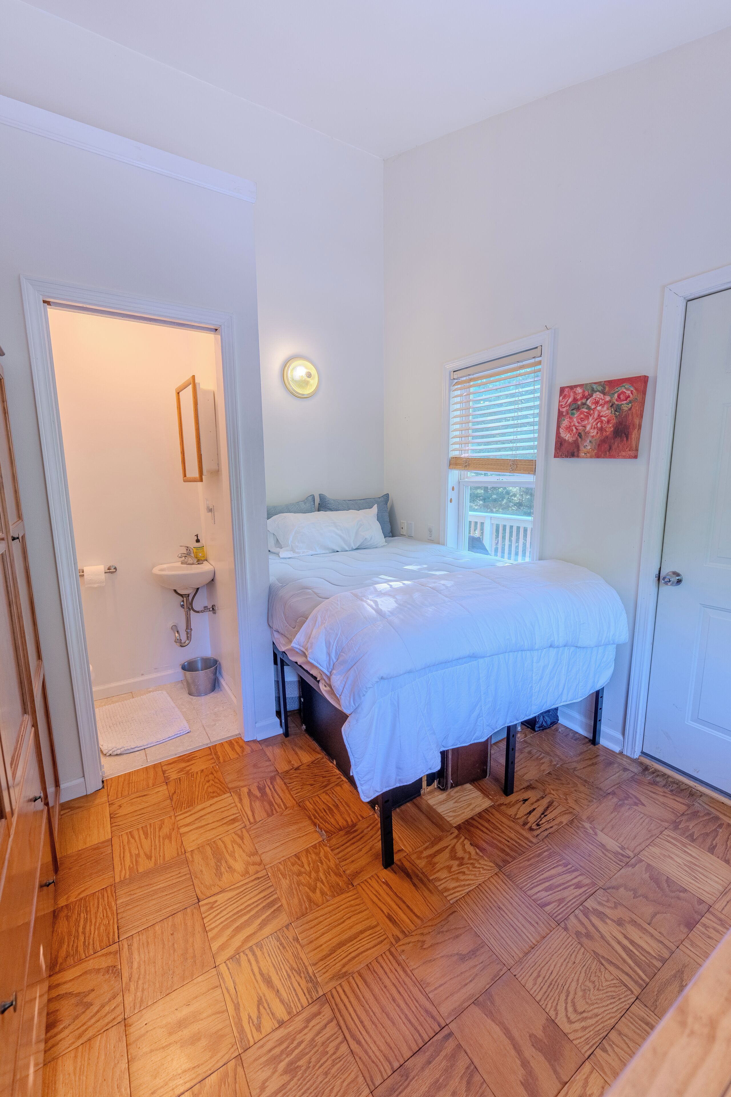 Une chambre à coucher avec un lit, une fenêtre avec des stores, un lavabo et une porte.