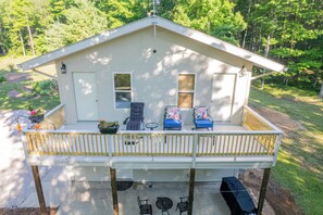 A two-story house with a covered porch, two chairs, a small table, and a potted plant. - White Pine Lodge: U.P. Fall Foliage Retreat | Private Sauna & 80 Acres | Sleeps 6 (Manistique)