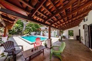 A covered outdoor area with a pool, chairs, and potted plants.