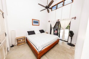 A bedroom with a bed, ceiling fan, window with curtains, and a picture on the wall.