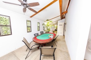 A room with a pool table, ceiling fan, and large windows.
