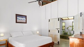 Une chambre à coucher avec un lit en bois, des lampes de chevet, un ventilateur de plafond et une porte donnant sur une autre pièce.