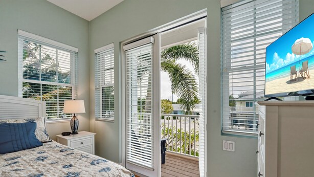 A bedroom with a bed, nightstand, lamp, and a TV displaying a beach scene. - Hidden Palms - Private Pool, Quiet Island Retreat Near Beach (Holmes Beach)