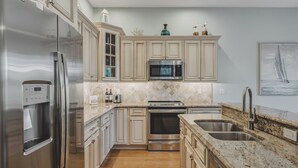 A modern kitchen with stainless steel appliances, light wood cabinetry, a granite countertop, and a large window. - Hidden Palms - Private Pool, Quiet Island Retreat Near Beach (Holmes Beach)