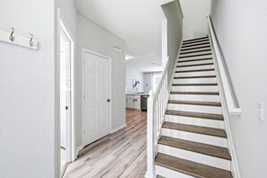 Ein Flur mit einer Holztreppe, weißen Wänden und einer Tür zu einem Küchenbereich.