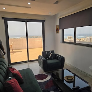 Ein Wohnzimmer mit einer Couch, einem Sessel, einem Couchtisch und einer großen Schiebeglastür, die auf einen Balkon führt.