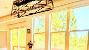 A dining area with a wooden table, four chairs, a hanging light fixture, and large windows with a view of trees. - The mountains are calling. Enjoy the perfect balance of serenity and adventure. (Westcliffe)