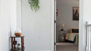 A hallway with a plant, a small table with a vase, and a doorway leading to a bedroom with a bed and a nightstand. - The mountains are calling. Enjoy the perfect balance of serenity and adventure. (Westcliffe)