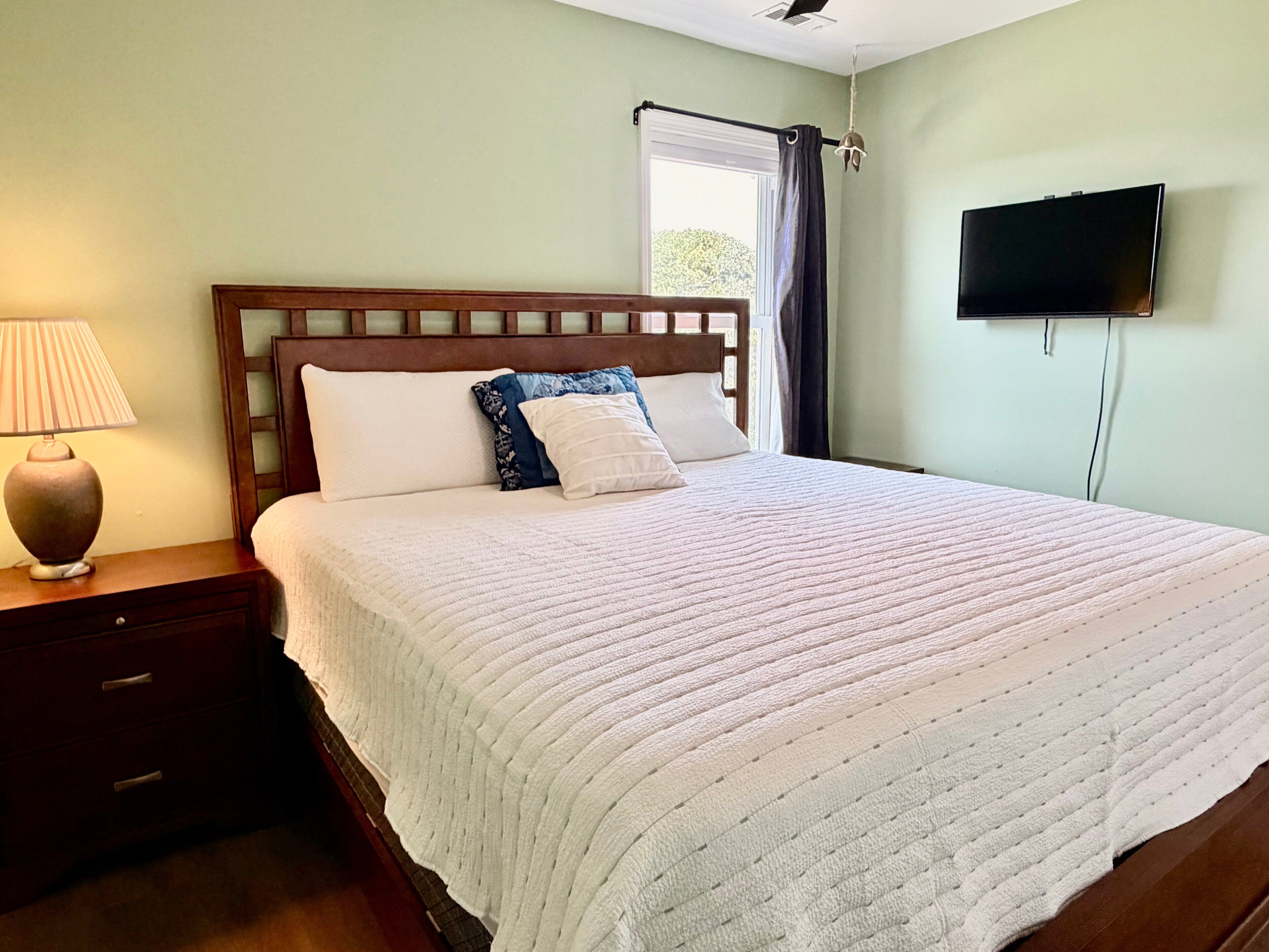 Un lit bien fait, avec une couette blanche, une tête de lit en bois et une table de chevet sur laquelle se trouve une lampe.