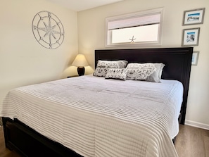 Una cama bien hecha con colcha blanca, cabecera oscura y almohadones decorativos.