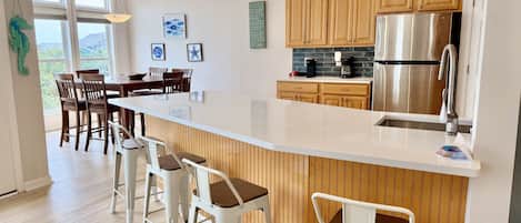 A modern kitchen with a large island, wooden cabinets, stainless steel appliances, and bar stools.