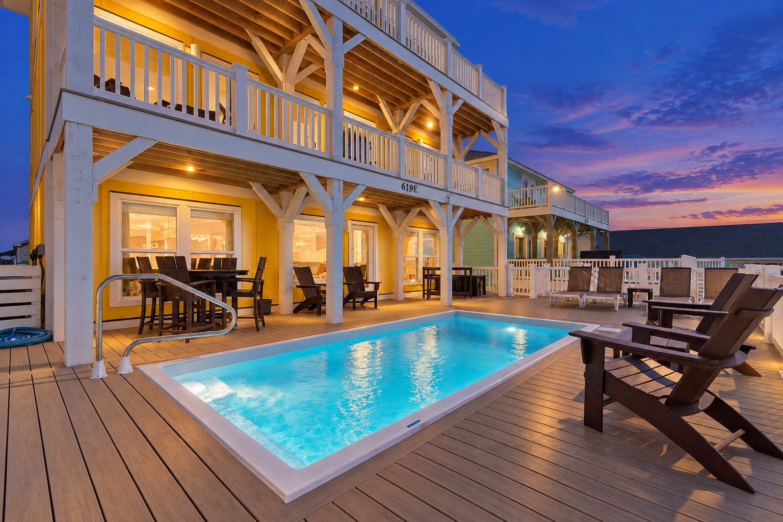 A multi-level outdoor deck with a swimming pool, seating areas, and a view of the ocean at dusk.
