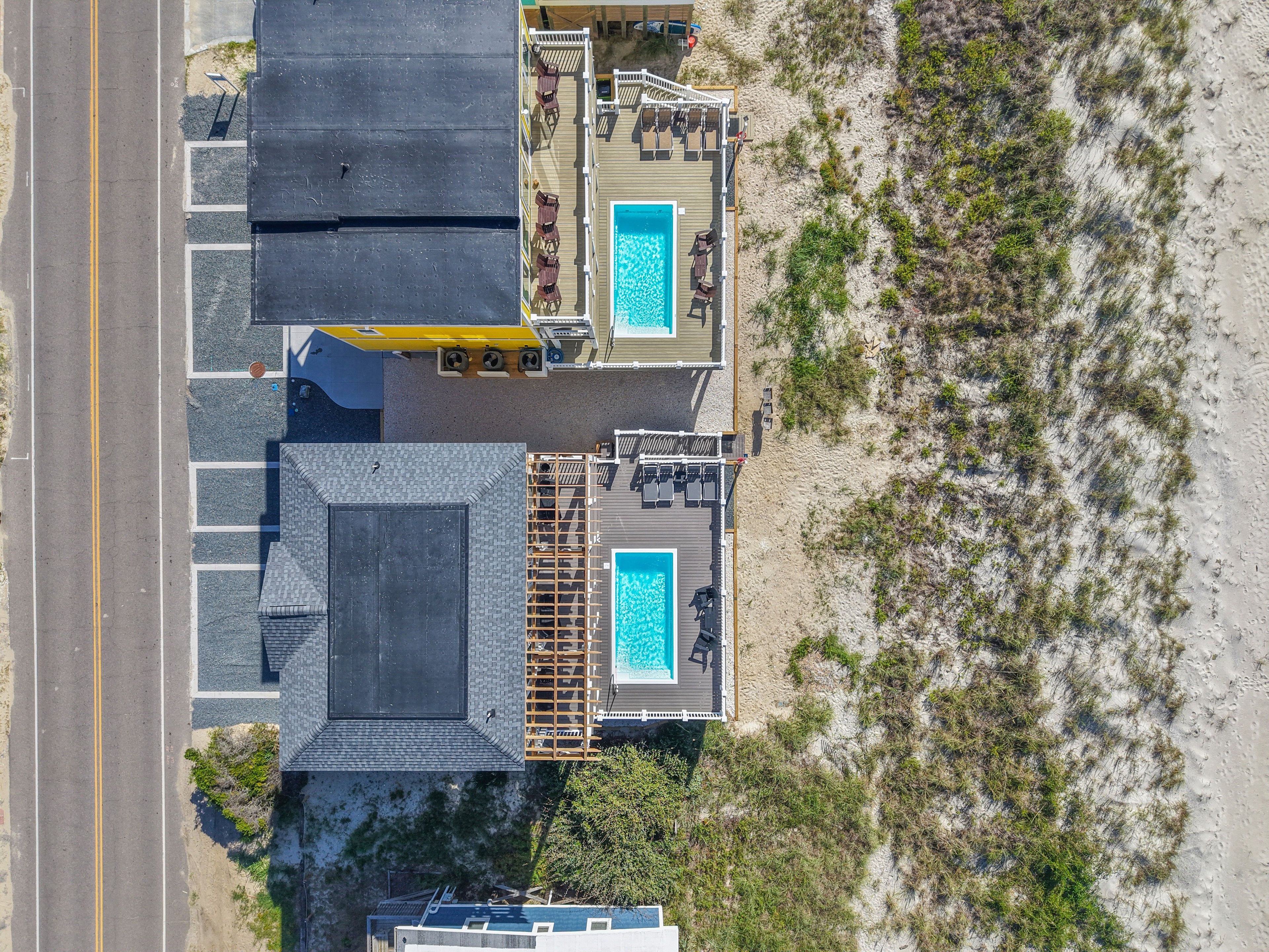Vue aérienne d’une propriété située en bord de mer, dotée de deux piscines, d’une terrasse couverte et d’une route adjacente.