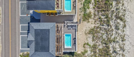 An aerial view of a beachfront property with two swimming pools, a covered deck area, and a road adjacent to the property.