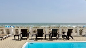 A poolside area with chairs and tables, a view of the ocean, and a white fence. - Oceanfront 8BR Oak Island home with private heated pool. (Oak Island)