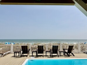 A poolside area with chairs and tables, a view of the ocean, and a white fence. - Oceanfront 8BR Oak Island home with private heated pool. (Oak Island)