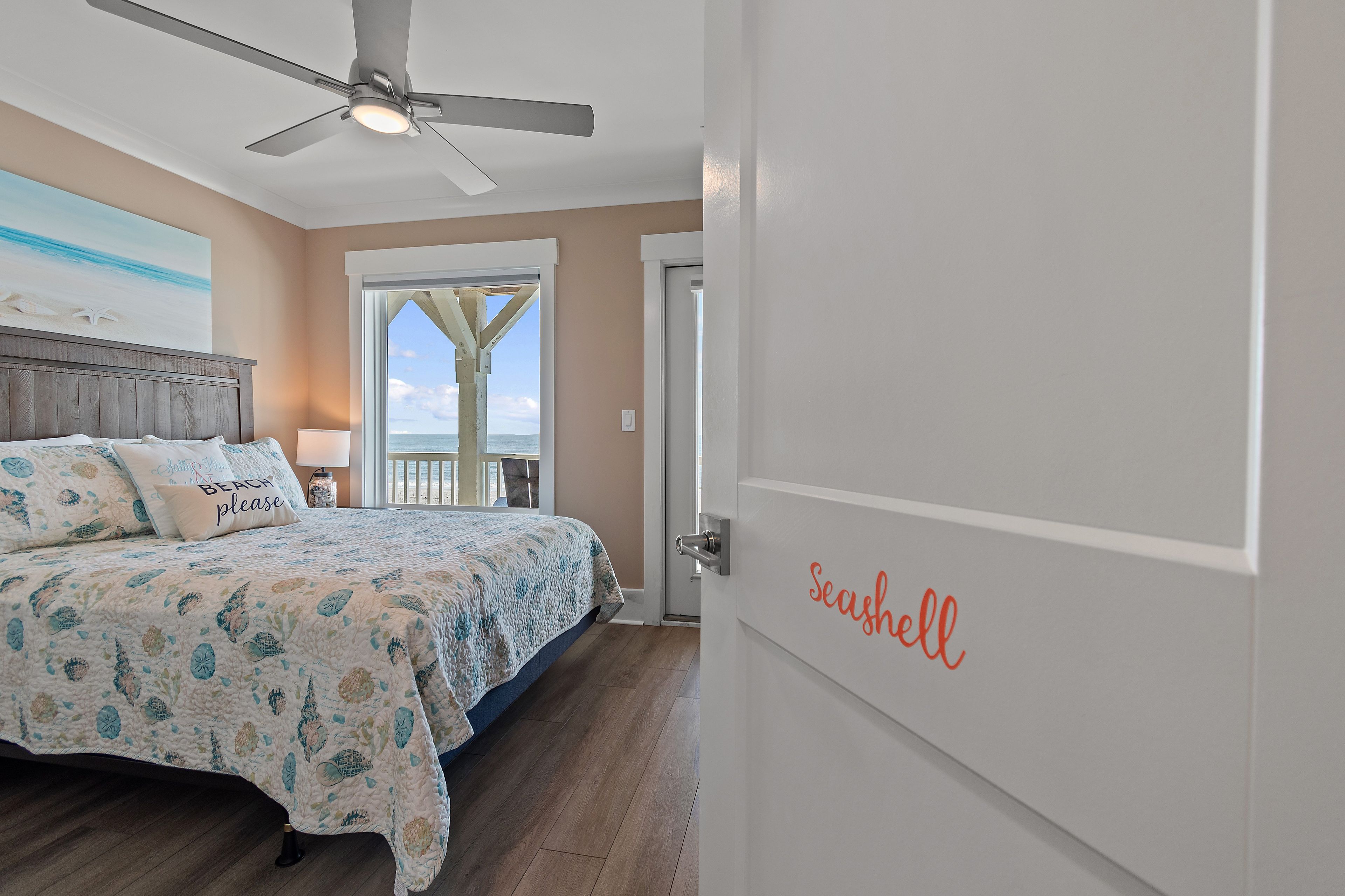 A bedroom with a bed, a ceiling fan, and a view of the ocean through a door.