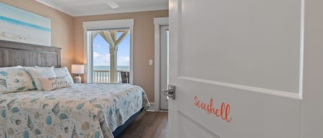 A bedroom with a bed, a ceiling fan, and a view of the ocean through a door.