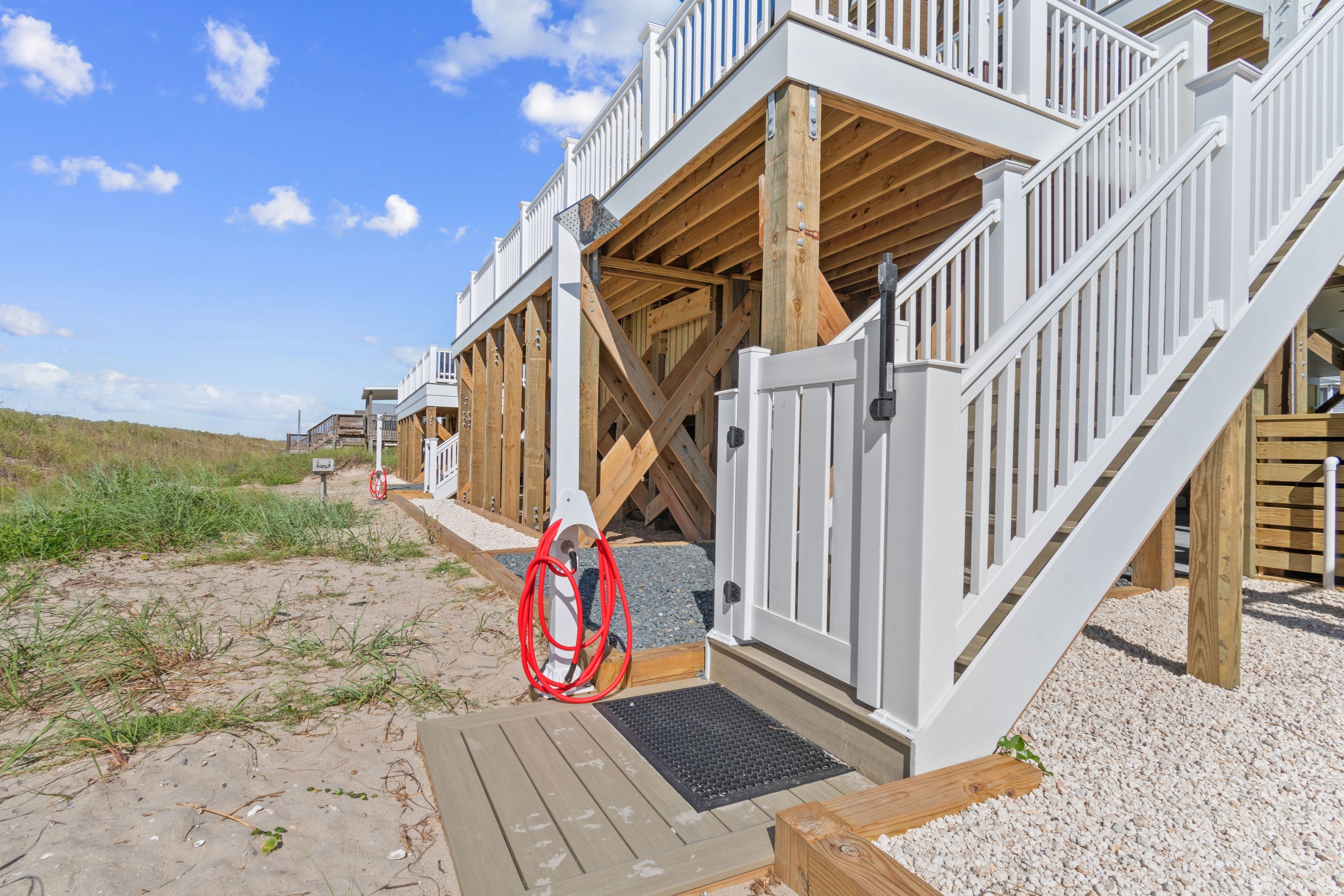 A beachfront property with wooden deck, white railings, and a red gate.
