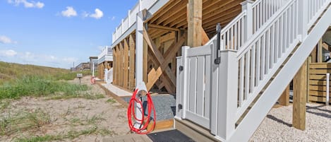 Een strandhuis met een houten terras, witte leuning en een rood hek.