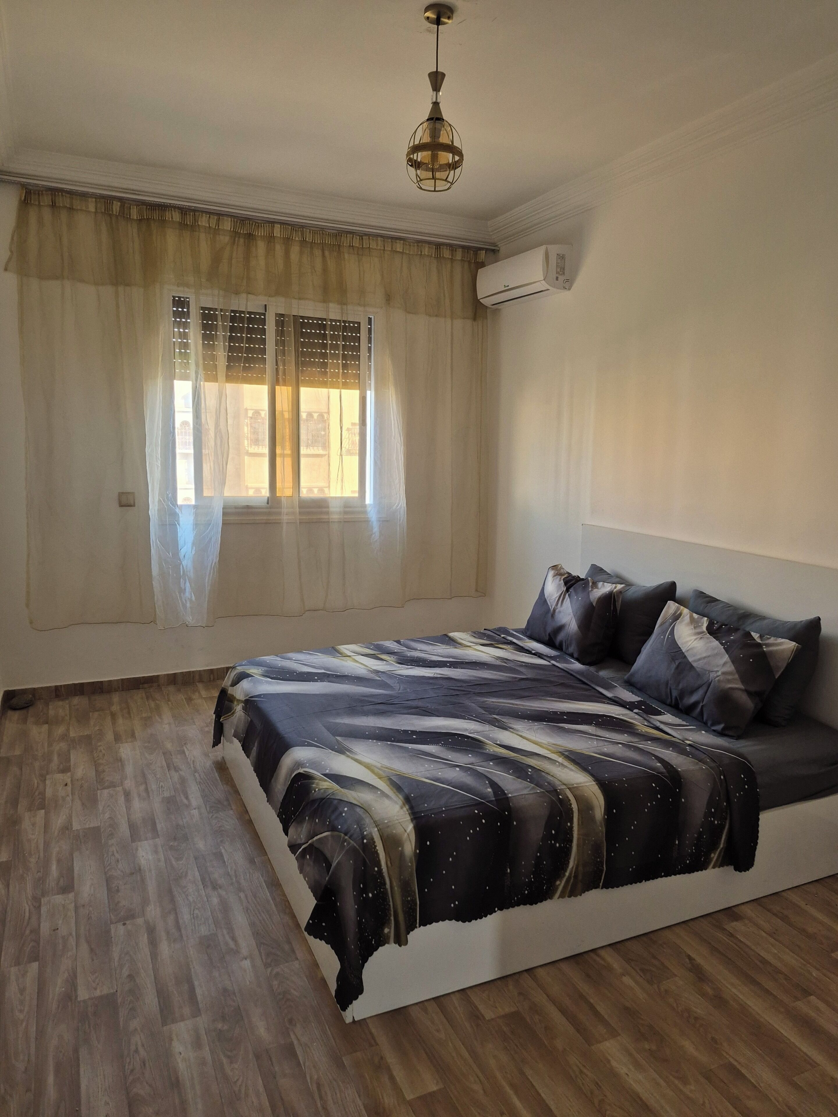 A bedroom with a bed, curtains, a window, and an air conditioning unit.