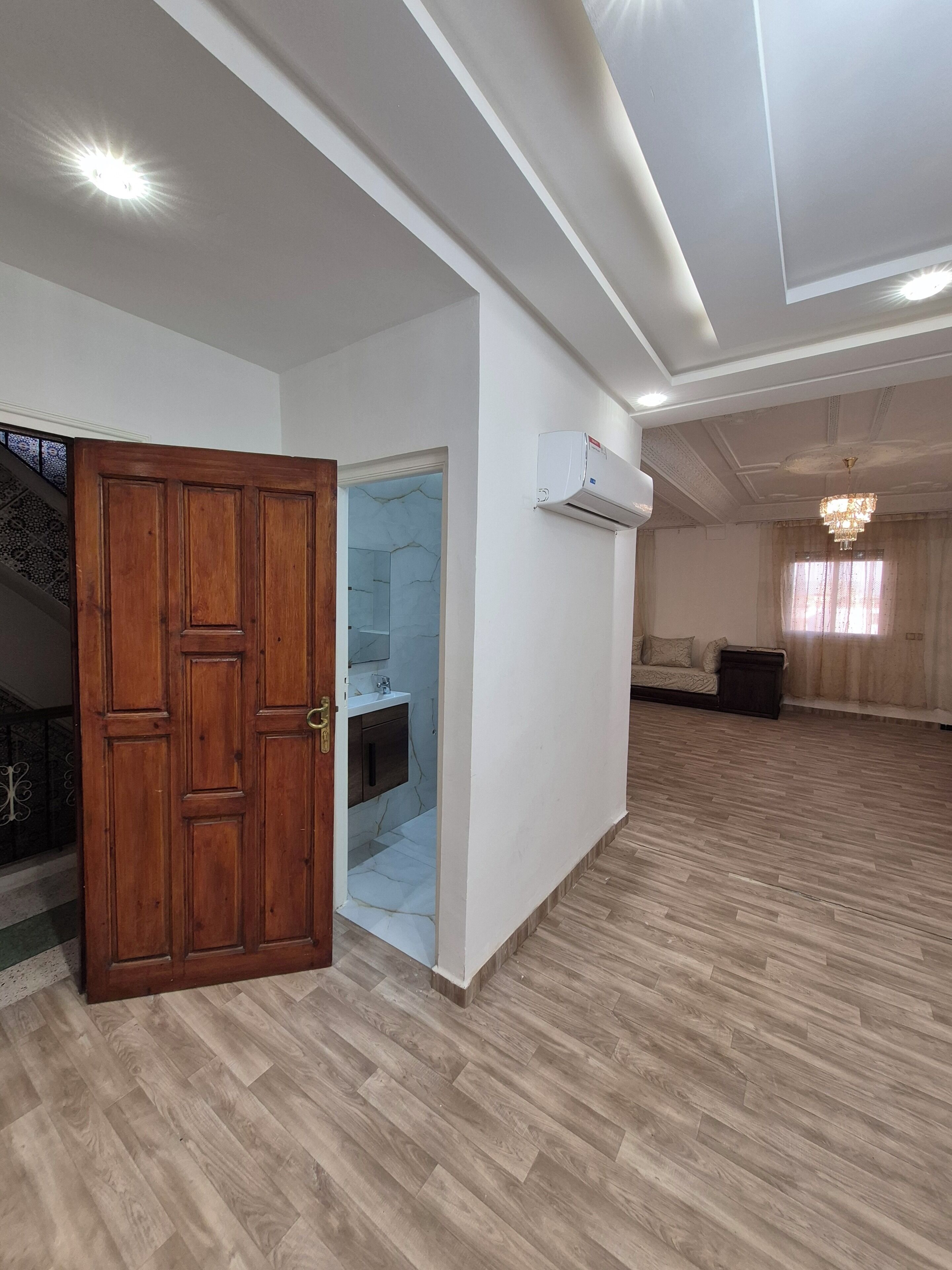 A spacious room with a wooden door, a built-in air conditioning unit, a chandelier, and a patterned floor.