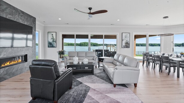 A spacious living room with a fireplace, a sofa, a dining area, and large windows overlooking a body of water. - Waterview Oasis | Pool & hot tub| Game Room | Outdoor Kitchen (Terrell)