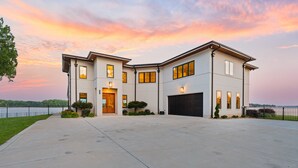 A modern two-story house with a large driveway, a garage, and a view of a lake. - Waterview Oasis | Pool & hot tub| Game Room | Outdoor Kitchen (Terrell)
