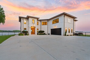 A modern two-story house with a large driveway, a garage, and a view of a lake. - Waterview Oasis | Pool & hot tub| Game Room | Outdoor Kitchen (Terrell)