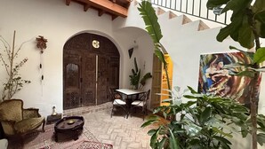 Un patio con una puerta de madera, una mesa con sillas y un cuadro en la pared.